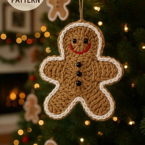 Op de afbeelding: Een gehaakte peperkoeken man kerstversiering met een witte rand, zwarte knoopogen en een rode glimlach, hangend aan een kerstboom. De tekst "DIGITAL CROCHET PATTERN" staat in een witte cirkel linksboven.