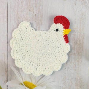 Può includere: Un sottobicchiere fatto a mano all'uncinetto bianco a forma di gallina, con cresta rossa e becco giallo. Il sottobicchiere ha un bordo smerlato e un occhio nero. Un'aggiunta affascinante a qualsiasi cucina o sala da pranzo.