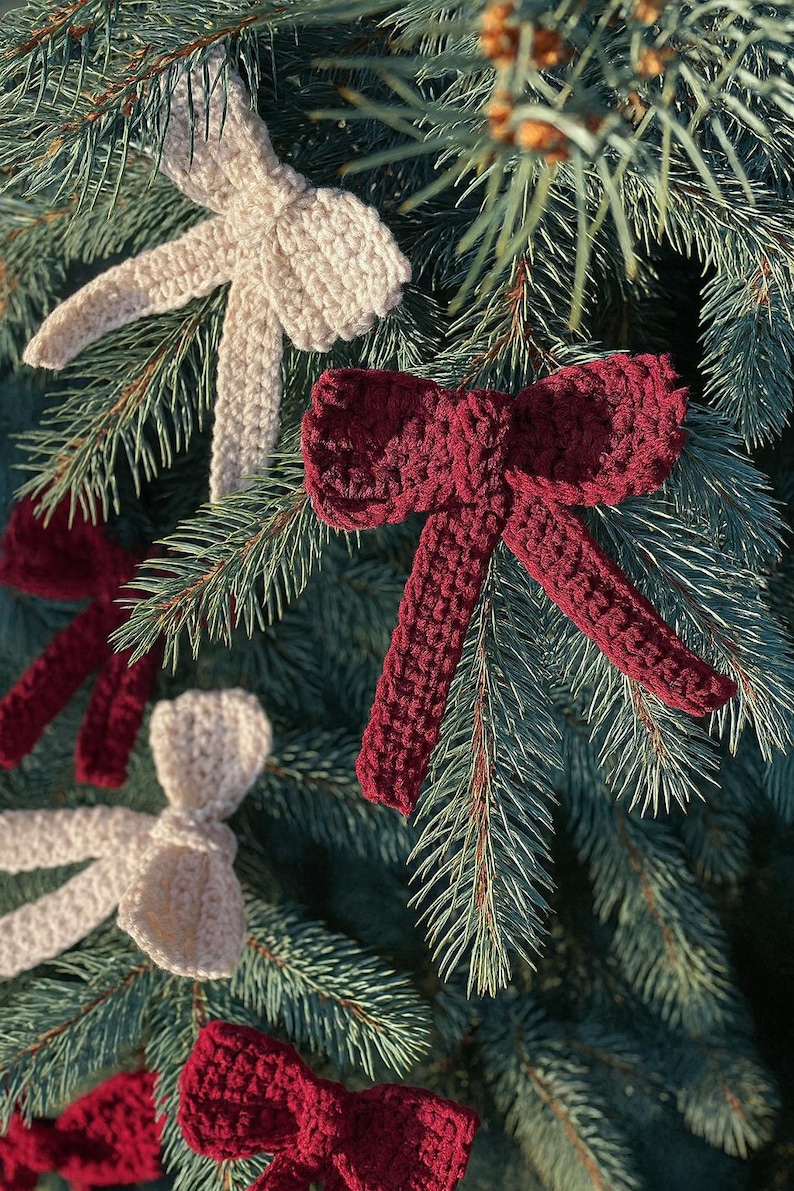 Op de afbeelding: Close-up van een kerstboom met verschillende handgemaakte gehaakte strikversieringen. De strikken zijn in cr&egrave;me- en bordeaux tinten en zijn bevestigd aan de groenblijvende takken. Een feestelijke vakantiedecoratie.