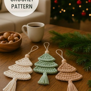 Könnte beinhalten: Drei handgefertigte Weihnachtsbaum-Ornamente aus Häkelarbeit in Creme, Grün und Beige, jeweils mit Quaste und Holzperle. Die Ornamente sind auf einer Holzoberfläche ausgestellt. Der Text "DIGITAL CROCHET PATTERN" ist enthalten.