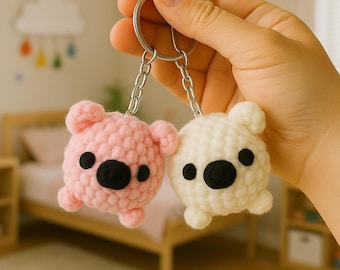 May include: Two handmade crochet bear keychains. One is light pink, the other is white. Both have black button eyes and noses. The keychains are held together by a silver chain and ring.