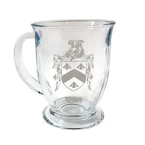 Może przedstawiać: Przezroczysty kubek szklany z uchwytem, z wygrawerowanym białym wzorem herbu z napisem "Walsh" poniżej.