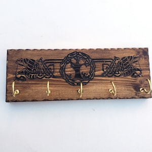 Puede incluir: Porta llaves de madera con un diseño de nudo celta y un motivo de árbol de la vida. Tiene cinco ganchos de latón para colgar llaves.
