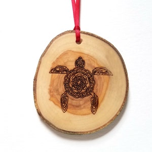 Könnte beinhalten: Ein Holzschmuckstück in Form eines Baumstamms mit einem keltischen Knotendesign einer Schildkröte, das in die Oberfläche gebrannt ist. Der Schmuck ist an einem roten Band befestigt.