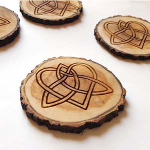 May include: Four wooden coasters with a Celtic knot heart design. The coasters are made of natural wood and have a rustic look.
