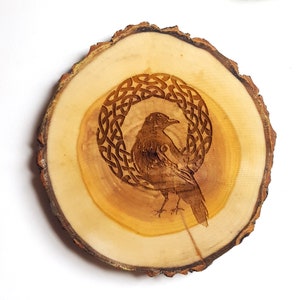 Op de afbeelding: Een houten onderzetter met een Keltisch knoopontwerp en een vogel in de knoop. De onderzetter is gemaakt van natuurlijk hout en heeft een rustieke uitstraling.