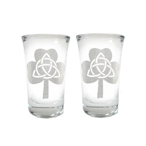 May include: Two clear glass shot glasses with an etched design of a shamrock with a Celtic knot inside.