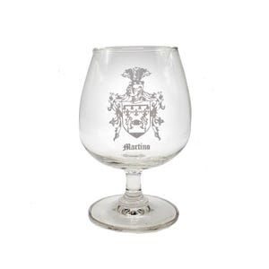 May include: A clear glass goblet with a stem and a round base. The goblet is engraved with a coat of arms and the name "Martino".