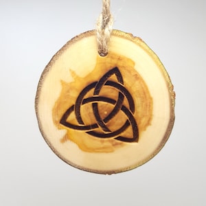 Könnte beinhalten: Ein Holz-Anhänger mit einem eingebrannten keltischen Knotenmuster. Der Anhänger ist rund und hat oben ein Loch zum Aufhängen.