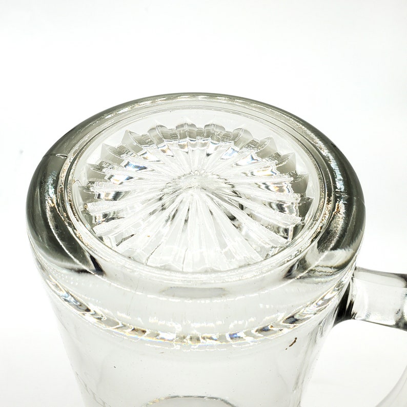 Puede incluir: Una taza de vidrio transparente con un dise&ntilde;o de estrella texturizado en la parte inferior. La taza tiene un asa y una forma redondeada.