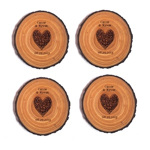 May include: Four round wooden coasters with a natural wood grain finish. Each coaster features a laser-engraved heart design with intricate details and the text "Cassie & Kevin" and "06.29.2013".