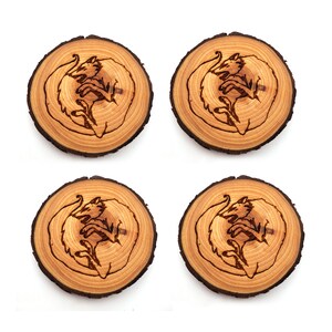 May include: Set of four wooden coasters featuring a laser-etched design of two wolves curled up together. The coasters are made from natural wood and have a rustic, organic look.