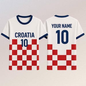 May include: A white short-sleeved t-shirt with dark blue trim on the collar and sleeves. The front features the text CROATIA above the number 10 and a red and white chequered pattern. The back displays the text YOUR NAME above the number 10.