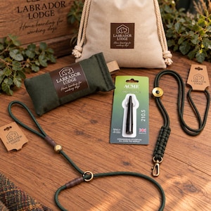 May include: A set of dog training gear including a beige drawstring pouch, a dark green canvas dummy, a black Acme 210.5 dog whistle on a card, and a dark green rope slip lead with brass hardware, all featuring Labrador Lodge branding.