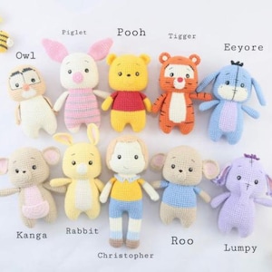 Puede incluir: Una colección de diez animales de peluche tejidos a ganchillo y una figura humana, incluyendo a Piglet, Pooh, Tigger, Eeyore, Owl, Kanga, Rabbit, Christopher, Roo y Lumpy, cada uno etiquetado con su nombre en texto negro arriba o abajo.