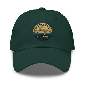 Könnte beinhalten: Dunkelgrüne Baseballkappe mit einem kreisförmigen Emblem mit einer Fischillustration, dem Wort "Rippletail" und dem Text "EST. 2025". Die Kappe hat einen gebogenen Schirm und einen Stoffriemenverschluss.