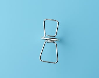 May include: A single, shiny, silver-colored metal clothespin against a solid light blue background. The clothespin has a simple, geometric design with two square-shaped ends connected by a coiled spring.