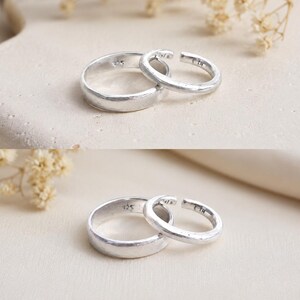 May include: Two silver-coloured rings with a textured, matte finish. One ring is a solid band, while the other is an open-style band. Both rings feature the hallmark 925 stamped on the interior surface, indicating sterling silver composition.