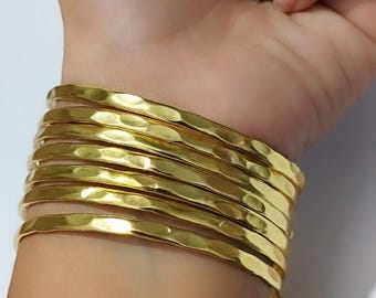 以下が含まれることがあります： ハンマー加工されたテクスチャの金色のバングルが手首を飾っています。 ブレスレットは重ねられており、大胆で人目を引くアクセサリーになっています。 ジュエリーは光沢のある反射性の金属で作られています。