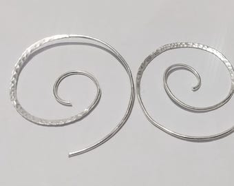 May include: A pair of silver spiral earrings. The outer spirals have a hammered texture, while the inner spirals are smooth. The design is a continuous line, creating a minimalist and elegant look. The earrings are displayed on a light grey background.