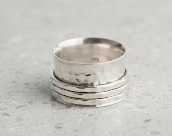 May include: A wide sterling silver spinner ring featuring a hammered, textured finish on the outer band. The interior of the ring is smooth and clearly stamped with the hallmark 925, indicating the silver content of this metallic jewellery piece.