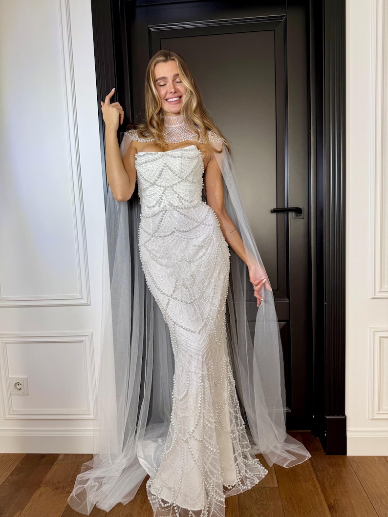 Ivory lace mermaid wedding dress with hand-placed pearls, strapless corset bodice and detachable sheer bridal cape.
