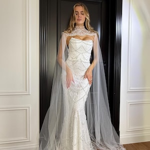 Luxury pearl wedding dress with mermaid silhouette, strapless corset and soft sheer cape creating a romantic bridal look.
