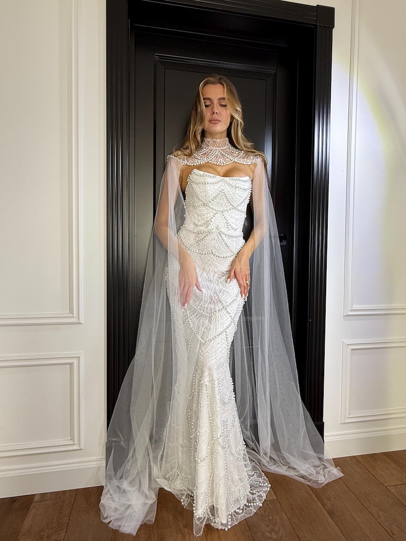 Luxury pearl wedding dress with mermaid silhouette, strapless corset and soft sheer cape creating a romantic bridal look.