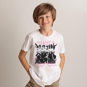 Pu&ograve; includere: T-shirt bianca con un design grafico. Il design presenta la parola "Dait" in rosa, insieme a un collage di volti e figure in bianco e nero. Il design &egrave; centrato sulla parte anteriore della maglietta.