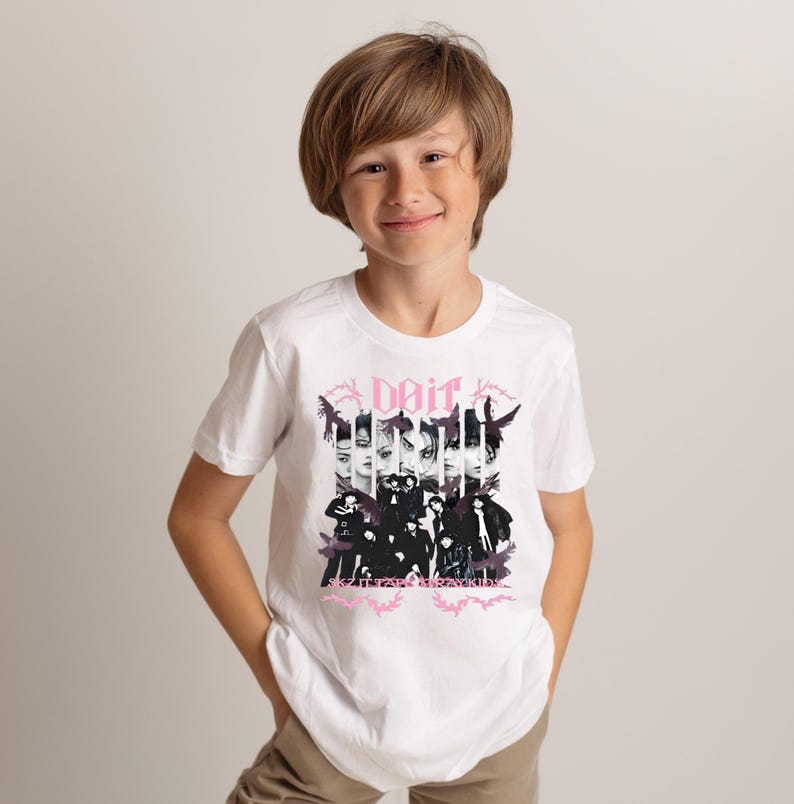 Pu&ograve; includere: T-shirt bianca con un design grafico. Il design presenta la parola "Dait" in rosa, insieme a un collage di volti e figure in bianco e nero. Il design &egrave; centrato sulla parte anteriore della maglietta.