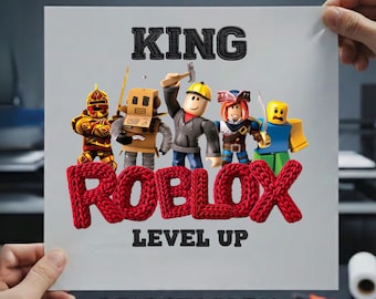 May include: A white sheet with the words "DTF TRANSFER" and "KING" in black. Below, the word "ROBLOX" is in red, with "LEVEL UP" beneath it. The sheet features cartoon characters and the text "READY TO PRESS".