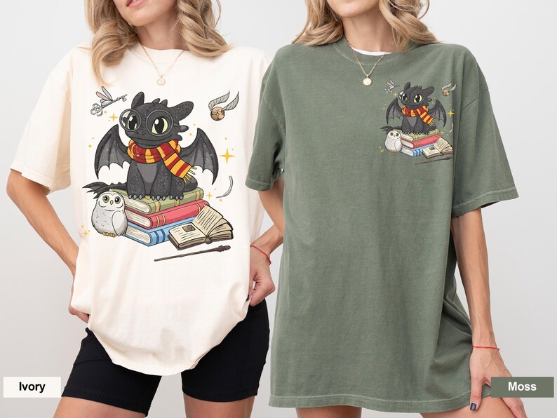 May include: Ivory and moss green t-shirts featuring a cartoon dragon with a scarf, sitting on books. The dragon is surrounded by a small owl, a wand, and other magical elements. The shirts are oversized and comfortable.