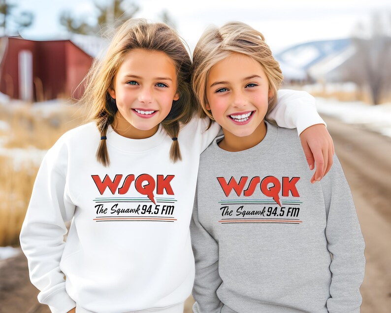 May include: Two young people wearing matching sweatshirts. One sweatshirt is white, the other is gray. Both sweatshirts have the text "WSQK The Squawk 94.5 FM" in red, black, and blue.