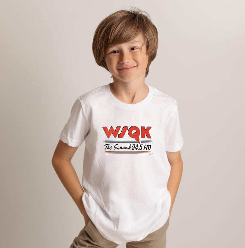 May include: A white t-shirt featuring the text "WSQK The Squawk 94.5 FM" in red and blue. The shirt has a crew neck and short sleeves. The design includes a red stylized "Q" and two horizontal lines.