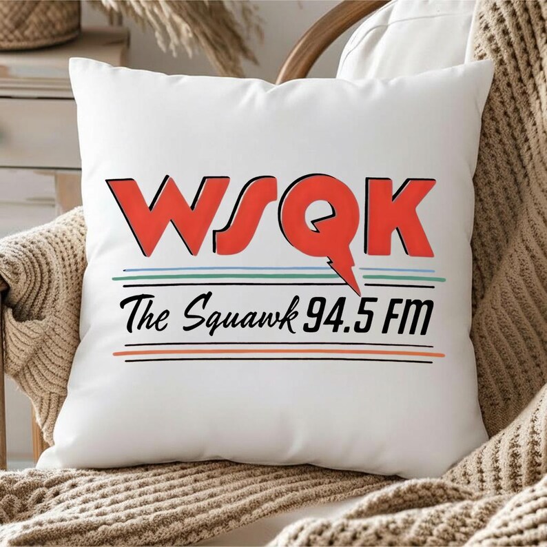 May include: White square pillow with the text "WSQK The Squawk 94.5 FM" in red and black. The pillow has a red lightning bolt design and is resting on a chair with a beige blanket.