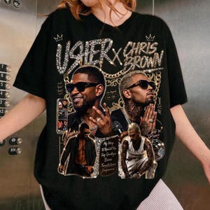 Pode incluir: Uma t-shirt preta com uma estampa gr&aacute;fica de Usher e Chris Brown. O design inclui detalhes de correntes douradas, coroas e o texto Usher x Chris Brown, My Way, U Remind Me, Say Goodbye, Burn, Translations e Confessions.