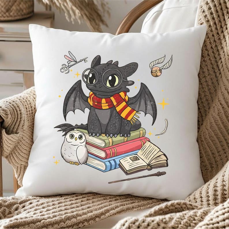 May include: White decorative pillow featuring a cartoon dragon wearing a scarf and glasses, sitting on a stack of books. An owl, a key, a golden snitch, and a wand are also depicted. The pillow is on a chair with a brown blanket.