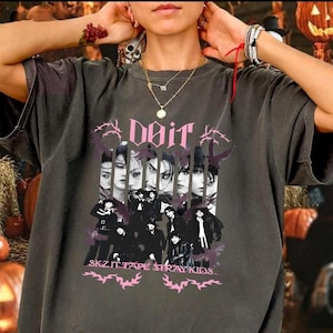 Pu&ograve; includere: T-shirt grigio scuro con una grafica rosa di un gruppo di persone e la parola "Doit". Il testo "SKZ IT TAPE STRAY KIDS" &egrave; in basso in rosa. La maglietta ha un aspetto vintage e usurato.