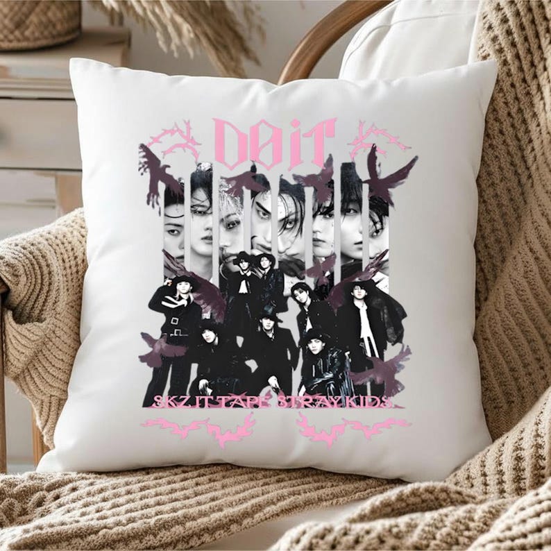 Pu&ograve; includere: Cuscino quadrato bianco con un design grafico rosa. Il design include la parola "Noir", immagini di persone e il testo "SKZ IT TAP STRAY KIDS" in rosa, insieme a sagome di uccelli scuri.