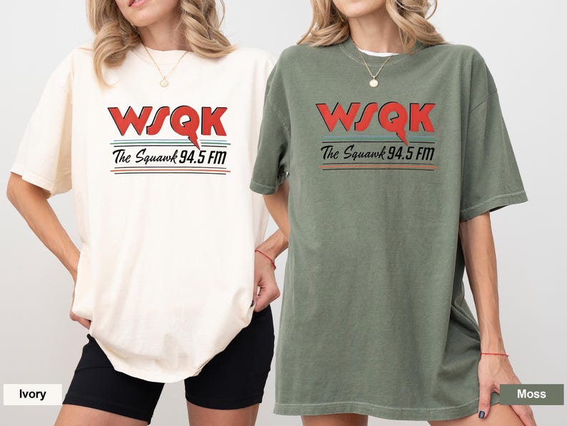 May include: Two short-sleeved t-shirts, one ivory and one moss green, each featuring the text "WSQK The Squawk 94.5 FM" in red, black, and teal. The shirts are a relaxed fit.