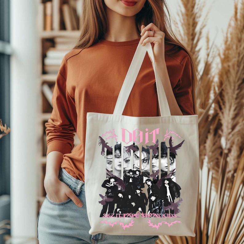 Pu&ograve; includere: Borsa tote color crema con un design grafico rosa con la parola "Doit", immagini di persone e il testo "SKZ IT TAPE STRAYKIDS". La borsa ha due manici lunghi.