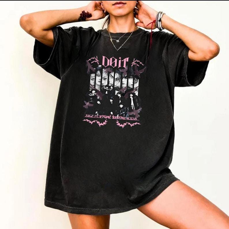 Pu&ograve; includere: T-shirt nera oversize con un design grafico. Il design include la parola "DOIT", volti e il testo "SKZ ITZY TWICE STRAY KIDS" in rosa. La maglietta ha maniche corte e una vestibilit&agrave; ampia.