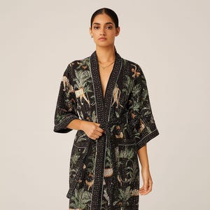 May include: Black robe with a jungle print featuring leopards, palm trees, and other foliage. The robe has a white trim and a matching belt. The robe is knee-length and has short sleeves.