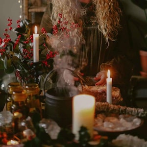 May include: A mystical scene featuring a black cauldron with steam rising, surrounded by candles, red berries, and glass jars. The warm lighting creates a cozy atmosphere, suggesting a ritual or spell-casting theme.