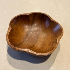 May include: A wooden bowl with a unique, flower-like shape. The bowl is made of a warm, medium-toned wood and has a smooth, polished finish. The bowl's design features rounded lobes, creating a natural and organic aesthetic. The bowl is empty and sits on a light-colored surface.