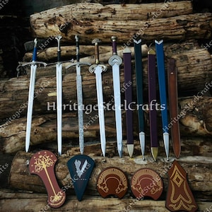 Könnte beinhalten: Sammlung von Schwertern und dekorativen Schilden, die auf einer rustikalen Holzoberfläche ausgestellt sind. Die Schwerter haben silberne Klingen und verschiedene Griffdesigns. Die Schilde sind braun und weisen komplizierte Muster und Symbole auf. Der Text "Heritage SteelCrafts" ist sichtbar.