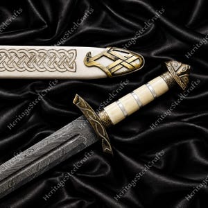 Può includere: Un pugnale con lama in acciaio Damasco a motivi, impugnatura color crema con anelli argentati e guardia color bronzo. Il fodero abbinato color crema presenta una punta in metallo color bronzo con un disegno inciso di uccello e intrecci.