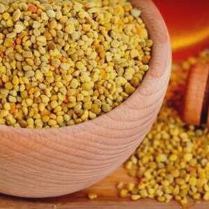 Può includere: Una ciotola di legno piena di polline d'api giallo. Un misurino di miele di legno e un mucchio di polline sono accanto alla ciotola. L'immagine ha un'estetica calda e naturale, che suggerisce un focus sui prodotti naturali per la salute.