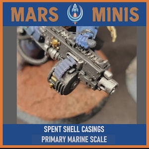 May include: A detailed miniature firearm with a dark metallic finish, featuring a drum magazine and intricate mechanical details. The image includes the text "MARS MINIS" and "SPENT SHELL CASINGS PRIMARY MARINE SCALE". The miniature is set against a brown backdrop.
