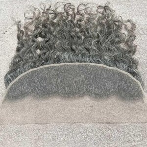以下が含まれることがあります： グレーのレースフロントウィッグ、カールヘア付き。ウィッグは自然なヘアラインと柔らかく質感のある外観が特徴です。髪はグレーとシルバーの色合いが混ざり合い、波状の質感です。